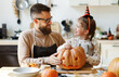 happy family   father and child girl prepare for Halloween by carving pumpkins at home in kitchen.
