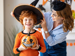 Wall Mural - happy family: mother laughs and helps the ginger son to put on a costume for the celebration of Halloween.