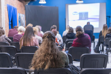 People sit in the room and listen to the speaker. View from the back. Concept - briefing, planning meeting, presentation. Selective focus, blur.