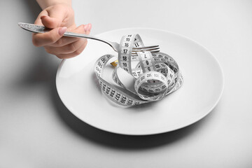 Female hand with plate, fork and measuring tape on grey background. Concept of anorexia