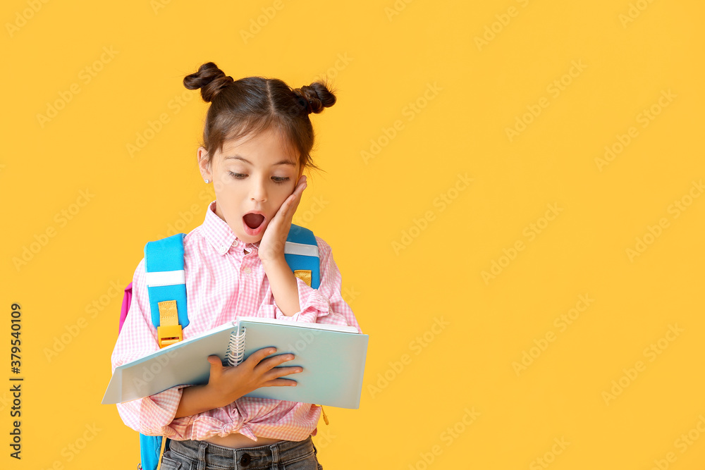 Surprised little schoolgirl with notebook on color background