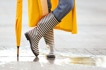 Beautiful young woman with umbrella wearing raincoat and gumboots outdoors