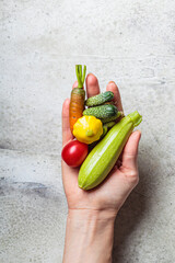 Wall Mural - Mini vegetables in hand. Mini zucchini, tomatoes, cucumbers, squash, and carrots on gray background.