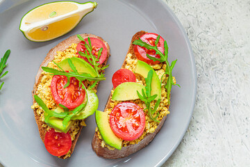 Wall Mural - Tofu scrambled sandwich with avocado, arugula and tomato on gray plate, top view. Healthy vegan food concept.