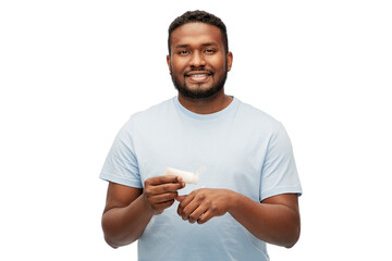 Wall Mural - grooming, skin care and people concept - happy african american man applying moisturizer to his hand over white background