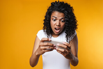 Wall Mural - Image of shocked african american woman playing video game on cellphone