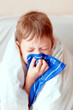 sick child with thermometer. boy with a runny nose. cold child in bed. boy blows his nose in a handkerchief