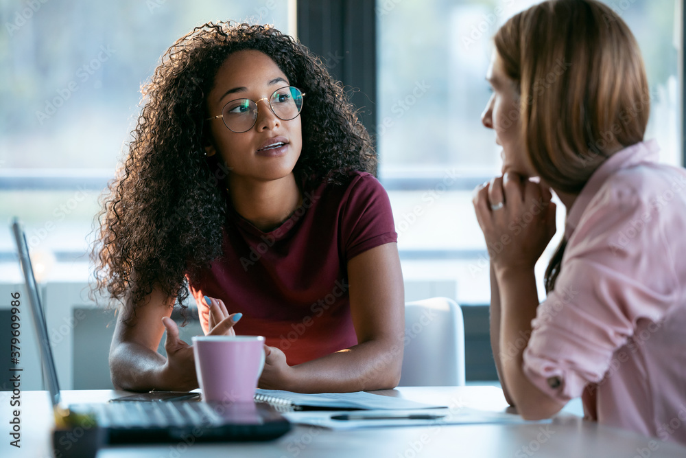 Two beautiful business women working together with laptop while talking about job news in the office.