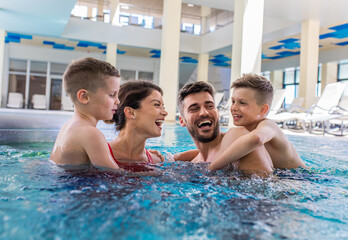 Wall Mural - smiling family of four having fun and relaxing in indoor swimming pool at hotel resort.