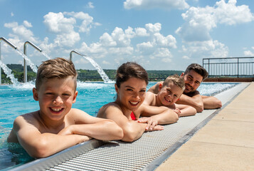 Wall Mural - portrait of smiling family of four having fun and relaxing in outdoor swimming pool at hotel resort.