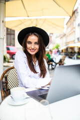 Wall Mural - Business woman using laptop at cafe. Young beautiful woman sitting in a coffee shop and working on computer