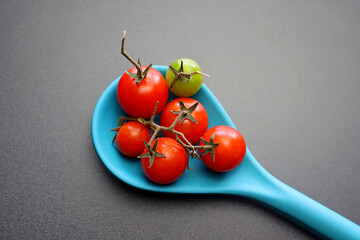 Wall Mural - Ripe red cherry tomatoes in a blue spoon on a gray background.