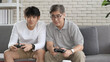 © Kiattisak - Asian two age generations men family old father embracing young adult son having fun enjoying play video game funny video using at home sit on sofa. Happiness Asian family concepts.