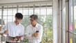 © Kiattisak - Young asian businessmen holding paper documents to discuss information with mature businessman holding a cup of coffee. Creative business people in modern office. Two men discussing marketing plan.