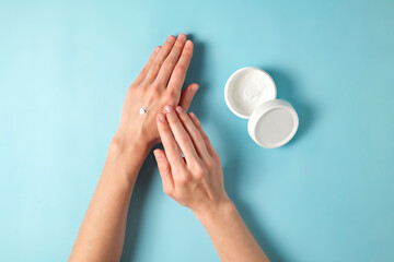 Wall Mural - Revitalizing hand cream for healing and recovery after excessive use of soap and disinfectants. Young woman applying moisturizing lotion. Copy space, close up, pink background, flat lay, top view.