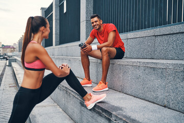 Wall Mural - Beautiful young couple in sports clothing warming up and smiling while practicing outdoors on the city street