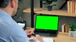 © viacheslav - Over the shoulder man teacher tutor at home office sits table with pen in hand talk speak with green screen laptop computer. Male teaches students by online remote conference web cam video call