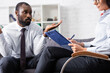 © LIGHTFIELD STUDIOS - selective focus of psychologist writing on clipboard near confused african american patient showing shrug gesture
