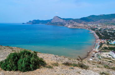 top view of resort town on shore of Black Sea bay among mountains and rocks, blue emerald water, summer, bush in the foreground