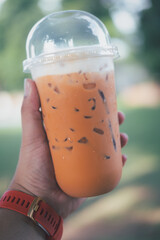 Iced Thai Tea in takeaway cup and fresh milk on top on man hand