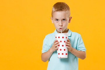 Wall Mural - Smiling little fun male fair-haired brown-eyed kid boy 5-6 years old wearing stylish blue t-shirt polo hold paper cup of drink cola soda isolated on yellow color wall background child studio portrait.