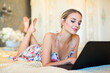 beautiful young woman lies on bed with laptop