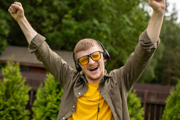 Joyful smiling man in headphones listen positive music with closed eyes, nature background. Summer holiday playlist, sounds of freedom travel inspiration dreams, winner concept. Copy text space