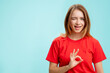 OK gesture. Perfect choice. Portrait of enthusiastic positive woman in red t-shirt accepting offer winking isolated on blue copy space commercial background. Great idea.