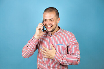 Russian business man over blue background having a conversation using smartphone over yellow background with a surprised face.