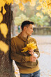 © anatoliycherkas - Handsome and happy guy with a bouquet of yellow leaves smiling and drinking coffee in autumn park