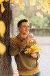 © anatoliycherkas - Handsome and happy guy with a bouquet of yellow leaves smiling and drinking coffee in autumn park