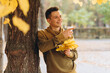 © anatoliycherkas - Handsome and happy guy with a bouquet of yellow leaves smiling and drinking coffee in autumn park