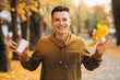 © anatoliycherkas - Handsome and happy guy with a bouquet of yellow leaves smiling and drinking coffee in autumn park