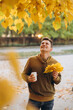 © anatoliycherkas - Handsome and happy guy with a bouquet of yellow leaves smiling and drinking coffee in autumn park