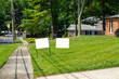 Two blank white signs on a green grassy lawn in a residential community