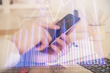 Double exposure of man's hands holding and using a digital device and forex graph drawing. Financial market concept.