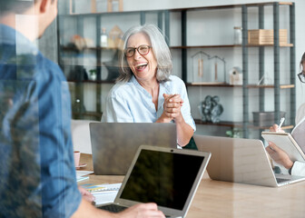 Happy mature old female mentor coach supervisor training young interns at group office meeting professional workshop. Cheerful middle aged teacher professor laughing with students at university class.