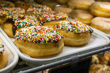 Bakery display case with freshly made doughnuts; glazed and chocolate frosted with sprinkles.