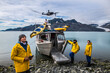 Man with crew members from scientific expedition  send a drone near the vessel docked on iceberg rock bay at wintertime to explore the island