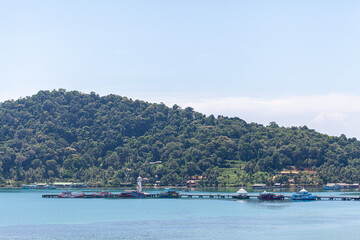 Beautiful summer landscape of the resort with turquoise sea water, village , hotels and mountains on the horizon, yellow flowers and blue sky. Thailand