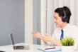 Work from home, Asian young businessman smile wearing headphones and suit video conference call or facetime on desk and raise his hand to explain to colleagues at home office