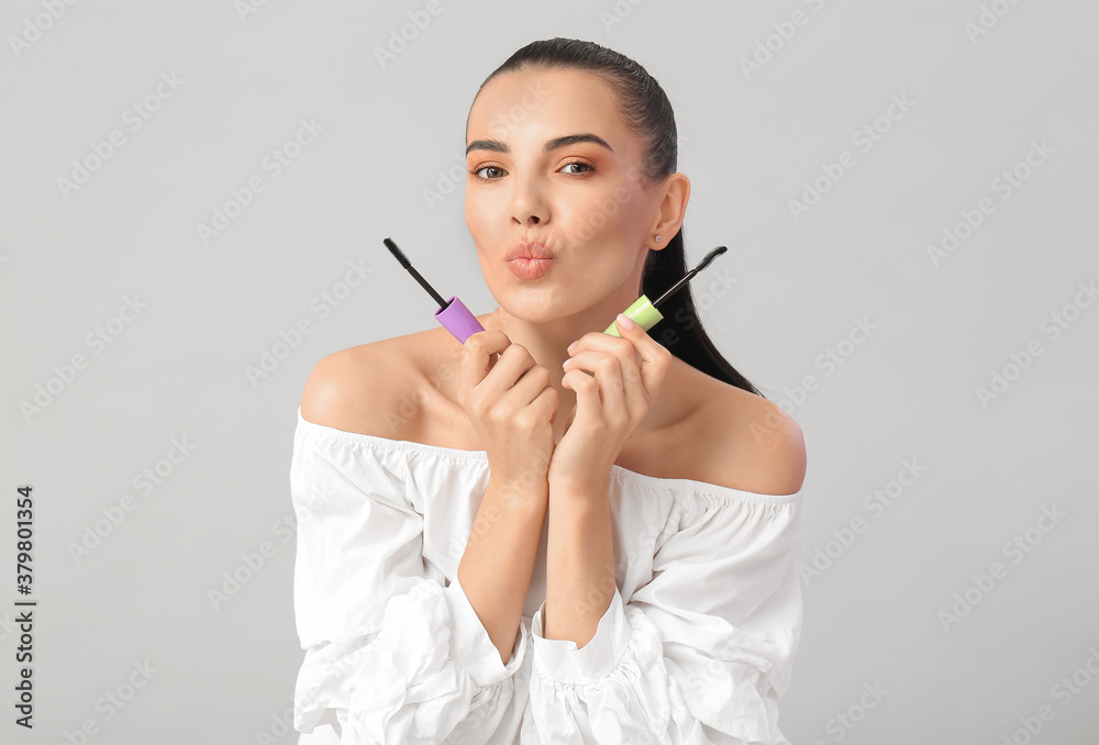 Beautiful young woman with mascara against light background