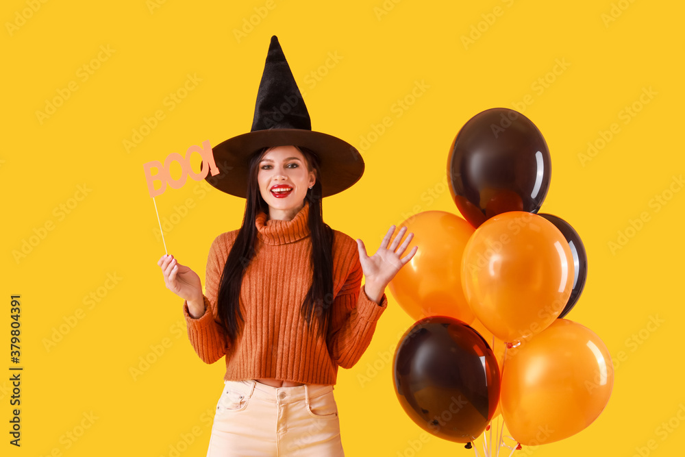 Beautiful young witch with balloons on color background. Halloween celebration