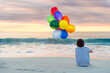 © Angela Lumsden/Stocksy - Boy sitting at the beach with a large bunch of colorful balloons