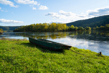 Wall Mural - River and old boat on shore in the mountains in autumn on a sunny warm day.