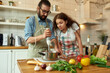 © Svitlana - Italian man, chef cook using hand blender while preparing a meal. Young woman, girlfriend in apron looking at the process, helping in the kitchen