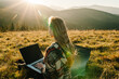 © Serhii - Woman traveler using laptop computer while enjoying sunset in mountains. Freelancer girl working on netbook during vacation holidays in autumn. Distant work and travel, freelance as lifestyle concept.
