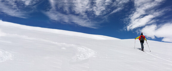 Wall Mural - man ski touring climbing snow-covered mountain under blue and cloudy sky