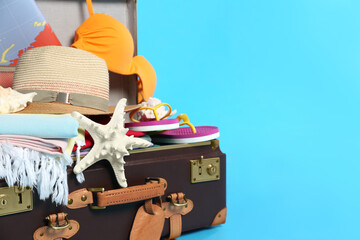 Wall Mural - Packed vintage suitcase with different beach objects on light blue background, space for text. Summer vacation