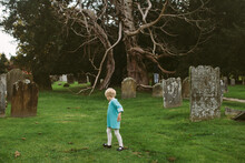 Anonymous Child In Vintage Dress Walks Through A Graveyard.